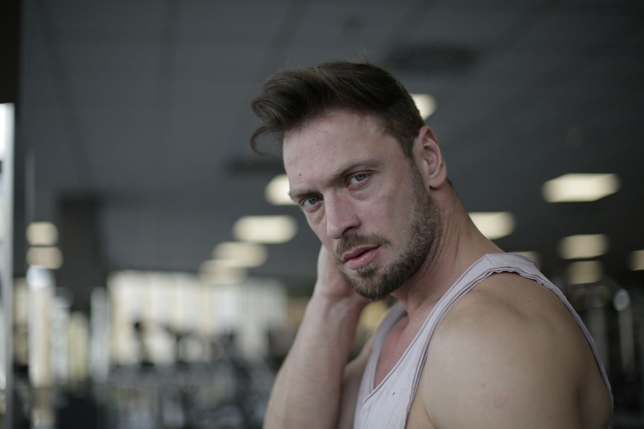 Close-up portrait of a pensive man with a beard and mustache in a gym setting.